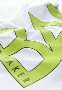 Hvid stof t-shirt med et stort grønt grafisk design med sorte konturer og ordet "BAKER." Glat tekstur med en afslappet pasform.