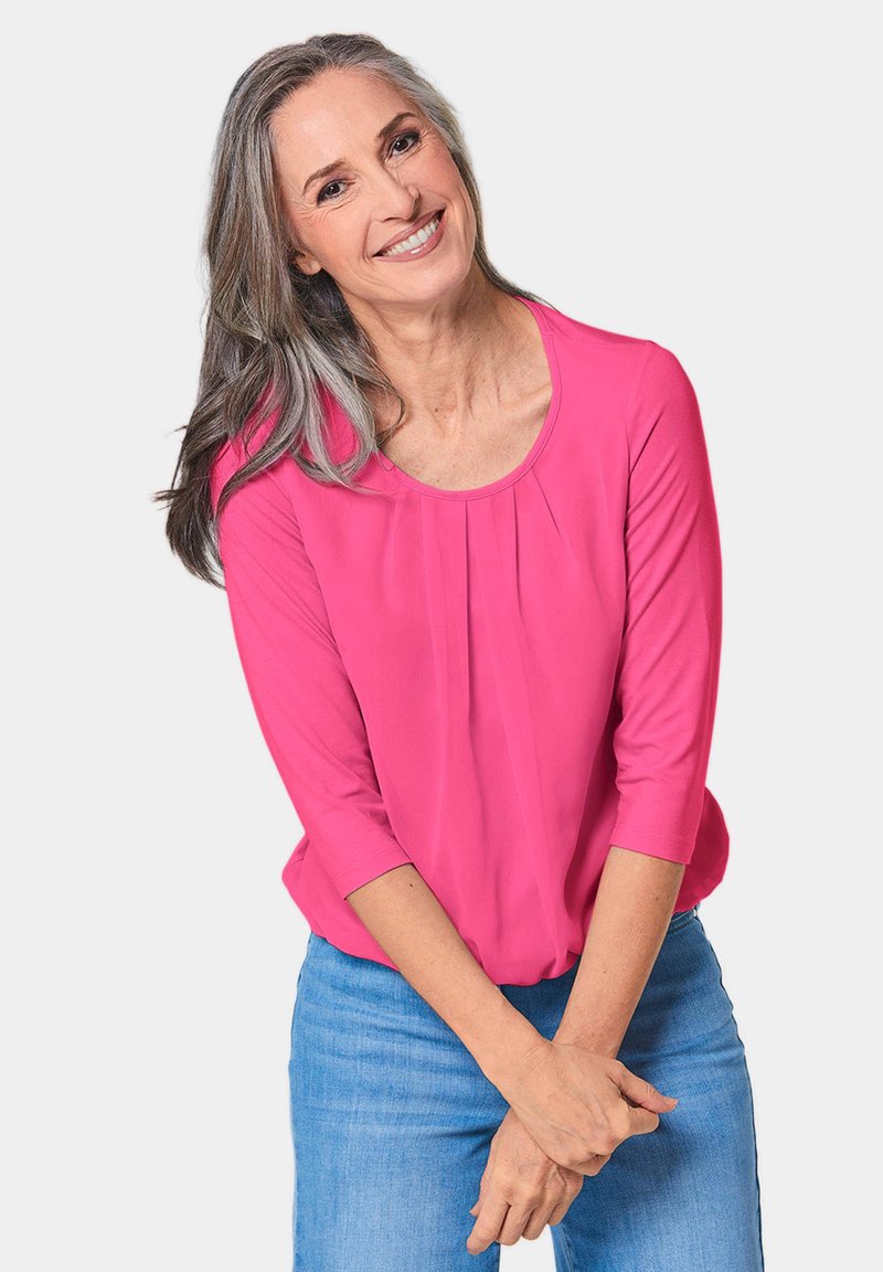 Rosa Langarmoberteil mit rundem Ausschnitt und vorderen Falten, kombiniert mit hellblauen Jeans. Geschmeidige Textur, lässiges Design.