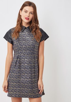 Vestido de marina con patrón floral dorado, mangas cortas de cuero negro, cuello puntiagudo y una silueta ajustada con un ligero vuelo.