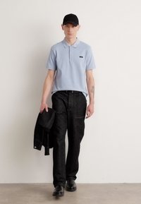 Polo bleu clair à manches courtes, pantalon noir et casquette noire. Le polo présente un petit logo et un tissu texturé.