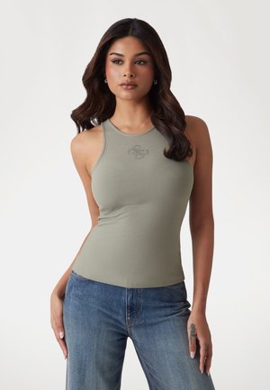 Débardeur côtelé sans manches en vert olive muted avec un col rond et un discret logo. Associé à un jean en denim bleu clair.