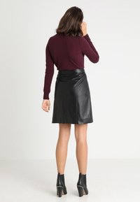 Burgundské pletené svetr spárované s černou koženou mini sukni, která má hladkou texturu a přiléhavý střih, doplněné kotníkovými botami.
