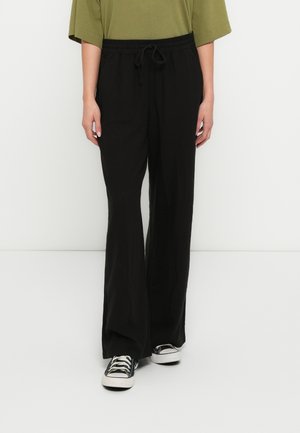 Black wide-leg pants with an elastic waistband and adjustable drawstring, paired with black sneakers, offering a relaxed fit.