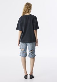 Dark gray oversized t-shirt with short sleeves, paired with distressed light blue denim shorts featuring large rips, and black chunky heels.