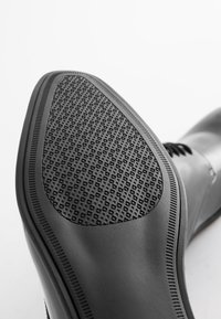 Black leather shoe with a textured rubber sole, featuring a patterned grip and smooth finish. The design is sleek with minimal stitching details.