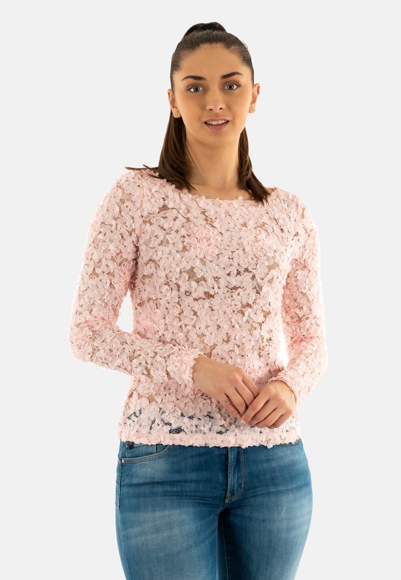 Maglietta a maniche lunghe rosa realizzata in pizzo floreale testurizzato con scollatura rotonda, abbinata a jeans blu. Presenta una silhouette aderente e un design trasparente.