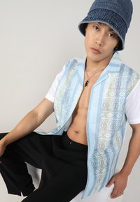 Chemise à manches courtes à motifs avec des nuances de bleu, vert et blanc, assortie à un pantalon noir. Présente une coupe décontractée et un col ouvert.