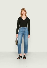 Sweater preto de malha canelada, jeans azul de cintura alta, sapatos de bloco abertos pretos, bolsa cinza com alça de corrente, design minimalista.