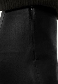 Czarna spódnica dżinsowa z eleganckim zamkiem z boku, gładką fakturą i dopasowanym krojem. Tkanina wydaje się lekko błyszcząca.