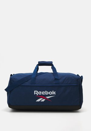 Mornarska torba s Reebok logotipom. Izrađena od izdržljive tkanine, s dvostrukim ručkama, podesivim remenom za rame i crnim dnom.