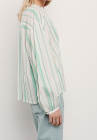 Blusa a righe bianca e verde menta con scollatura rotonda, maniche lunghe a sbuffo e polsini elasticizzati. Tessuto morbido e vestibilità comoda.