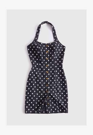Robe noire à col halter avec pois blancs, fermeture à boutons sur le devant et silhouette ajustée, posée à plat sur un fond blanc.