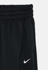 Zwarte sportieve broek met een elastische tailleband, zijzakken en een wit Nike-logo aan de linkerkant. Glide stofstructuur.