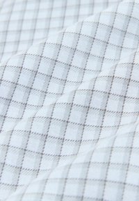 Valkoinen kangas, jossa on hienovarainen harmaanvaaleiden viivojen ruutukuvio, näyttää sileältä ja pehmeiltä laskoksilta.