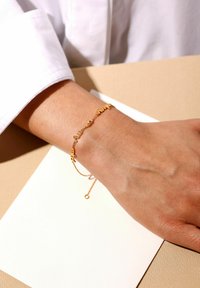 Gullarmbånd med sammenkoblede tekstcharms. Designet inkluderer fine led og en delikat justerbar kæde med spænde.