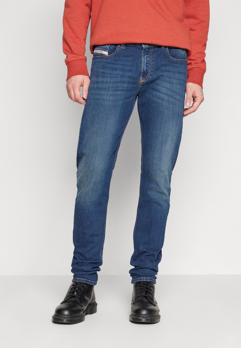 Jeans de mezclilla azul con corte ajustado, que cuentan con un diseño clásico de cinco bolsillos, detalles de costura y desgaste. Combinados con botas negras.