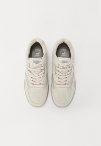 Ein Paar beiger FILA-Sneaker mit weißen Schnürsenkeln, genähten Details und Perforationen, von oben auf einem schlichten weißen Hintergrund gezeigt.