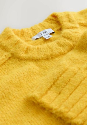 Kollane kudumisweater, millel on ribbed struktuur, ümmargune kaelus ja "NEXT" silt. Pehme, karvane lõng, mis tundub mugav.