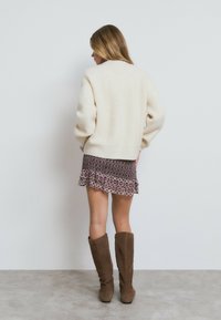 Suéter de punto crema, falda mini floral con capas y volantes, y botas altas de ante marrón. Textura notable y patrones contrastantes.