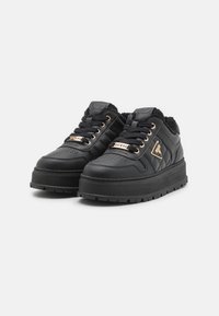 Sneakers neri con tomaia in pelle testurizzata e rivestimento in pelliccia sintetica, con occhielli dorati e dettagli del logo sul lato e sulla linguetta.