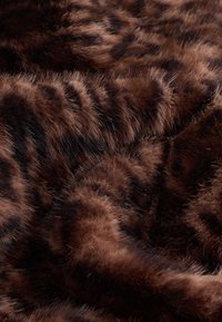 Primo piano di pelliccia animale morbida, densa, a strisce marroni e nere con una texture soffice e variazioni naturali del motivo.