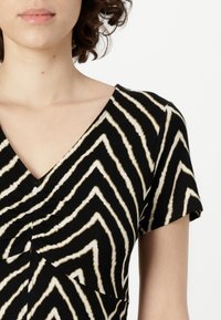 Svart-hvit mønstrete topp med korte ermer; har V-hals og sikksakk-striper som gir tekstur og visuell interesse til stoffet.