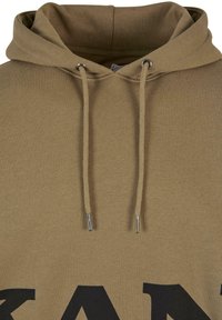 Felpa beige con una grande stampa di lettere nere, dotata di cappuccio con cordino e cordini con punta metallica. Tessuto morbido e strutturato.
