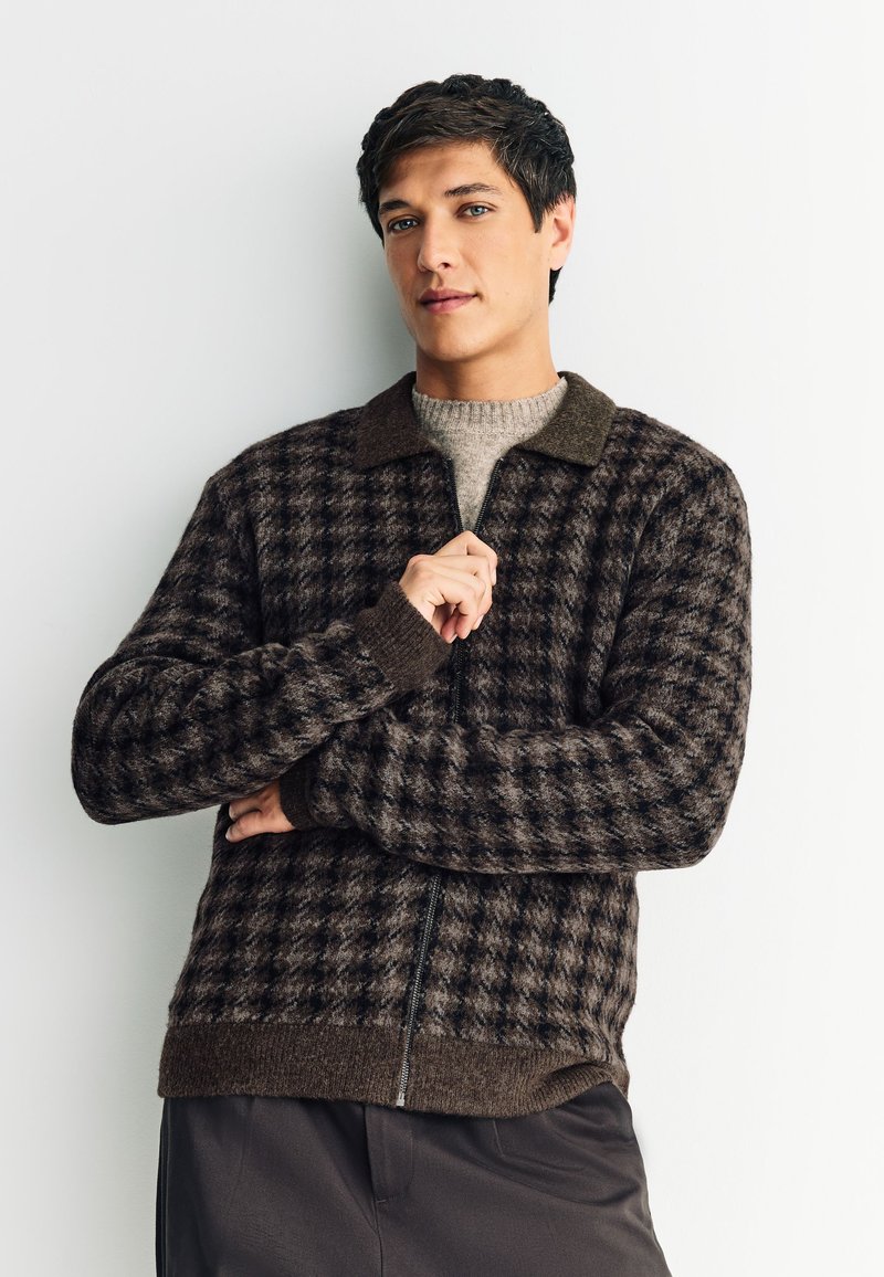 Veste zippée à carreaux marron avec col et poignets foncés. Confectionnée en tissu texturé, présentant un motif et un ourlet côtelé.