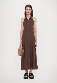 Brun lin maxi-kjole med knappestolpe, krage og uten ermer-design. Kombinert med en vevd kurvveske og platåsandaler.