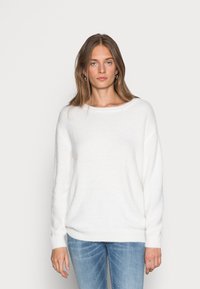 Valge, pehme kampsun laia kaelusega ja langetatud õlgadega. Pehme tekstuur, pikad varrukad ja mugav istuvus. Kantud helesiniste teksadega.