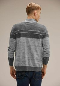 Šedý pruhovaný cardigan vyrobený z pleteného materiálu. Má stojací límec, dlouhé rukávy a vroubkované manžety. Obsahuje tmavší pruh přes zadní část.