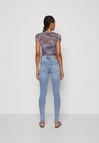 Grå tie-dye kortermet topp kombinert med lyseblå tettsittende jeans. Jeansene har baklommer og en liten brun etikett på livet.