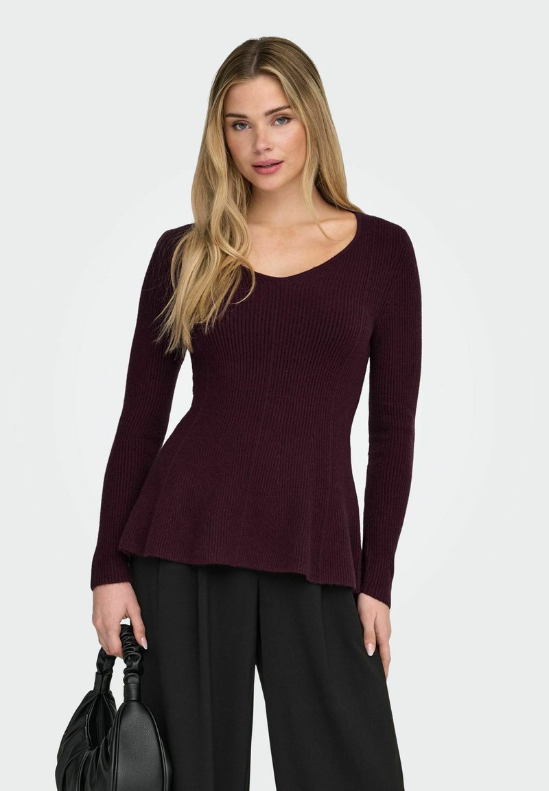Maglione bordeaux in maglia a coste con scollo a V, maniche lunghe e orlo svasato. Abbinato a pantaloni neri e una borsa nera dalla texture lavorata.
