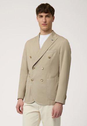 Beige double-breasted jacket with gold buttons, notch lapels, and two front pockets. Smooth fabric with a tailored fit and subtle stitching details.
