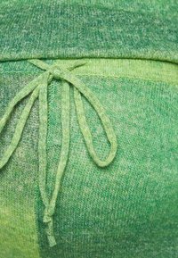Calças de moletão verdes em malha com uma textura em degradê, apresentando uma cintura com cordão. O material parece suave e leve.