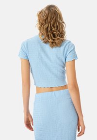 Top corto azul con acabado texturizado y mangas acampanadas, combinado con una falda de cintura alta a juego. Tejido suave y ligero.