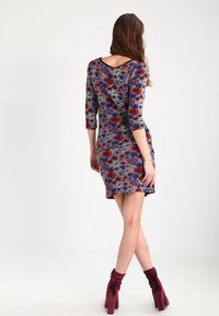 Veelkleurige jurk met een bloemenpatroon, ronde halslijn, driekwartmouwen en een aansluitende pasvorm, gecombineerd met bordeauxrode knielaarzen.