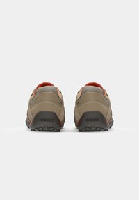 Beige atletik sko med mesh-paneler, teksturert ruskinn, røde detaljer og gummisåler, med en logo på hælen og en polstret krage.