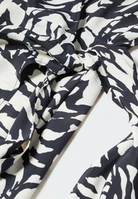 Černobílá látka s vzorem a hladkým povrchem, obsahující detaily vázání a splývavý design, uspořádaná v jemných záhybech.
