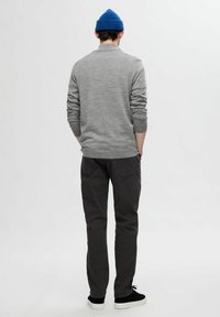 Grå tröja med långa ärmar, i kombination med mörka byxor och svarta sneakers. Personen bär en blå mössa, sedd bakifrån mot en enfärgad bakgrund.