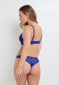 Soutien-gorge en dentelle bleue et string assorti avec un motif floral. Le soutien-gorge est doté de fines bretelles et d'un fermoir ajustable à l'arrière.