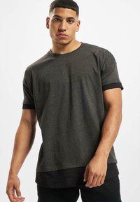 Dunkelgraues Kurzarm-T-Shirt mit einem schwarzen Rundhalsausschnitt und Ärmeln, gerader Schnitt und weicher Textur. Getragen mit einem schwarzen Unterhemd.