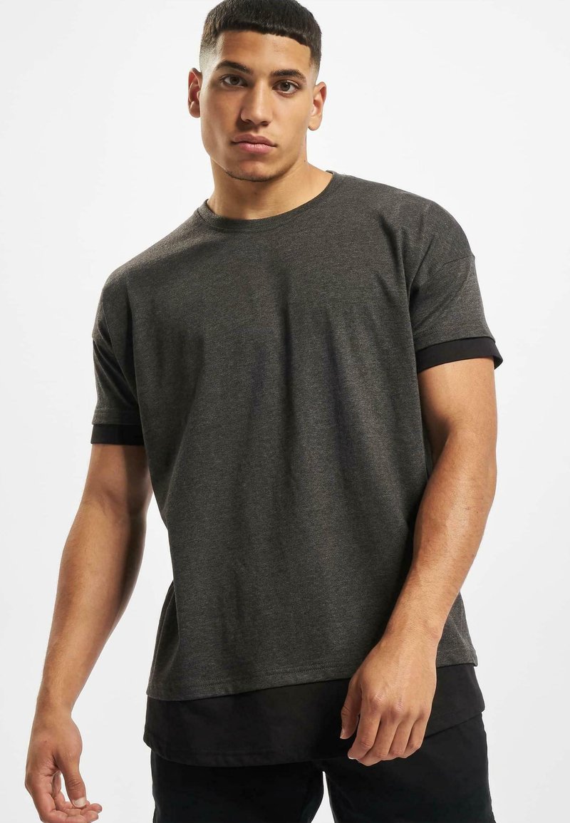 Dunkelgraues Kurzarm-T-Shirt mit einem schwarzen Rundhalsausschnitt und Ärmeln, gerader Schnitt und weicher Textur. Getragen mit einem schwarzen Unterhemd.