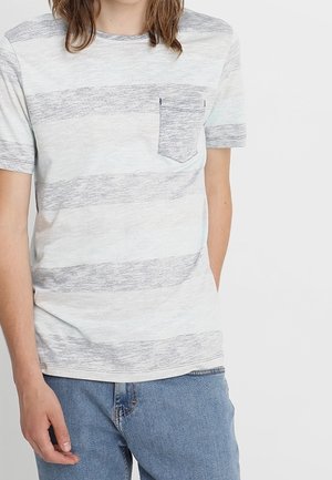 Osoba ubrana w jasnoszary i biały paskowany krótki rękaw koszulę z kieszenią na piersi oraz niebieskie dżinsy, na jednolitym białym tle.