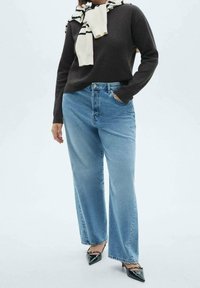 Mørkebrun sweater, lyseblå brede jeans og sorte spidse hæle. Tørklæde draperet omkring halsen med striber. Glatte teksturer.