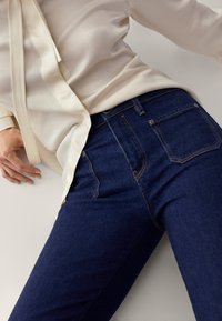 Mörkblå denimjeans med en mjuk textur, högmidja och två bakfickor. Matchas med en ljus, silkeslen krämfärgad blus.