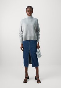 Ljusgrå stickad polotröja, denim midi kjol med slits framtill, svarta blockklacksandaler och liten blå handväska.