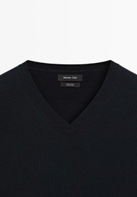 Maglione V in cotone 100% di colore blu navy scuro; presenta una texture a costine e un'etichetta con il marchio e le istruzioni per la cura all'interno del collo.