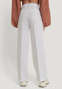 Białe lniane spodnie szerokie w nogawkach z wysokim stanem, o gładkiej teksturze i detalach w postaci guzików, zestawione z beżowymi trampkami.