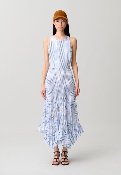 Donna che indossa un vestito midi plissettato senza maniche azzurro chiaro a pois, cappello marrone e sandali neri con cinturini e dettagli a forma di cuore dorati.